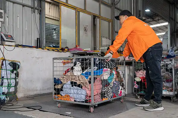 sorter compiling handpicked used clothes on a cart for baling