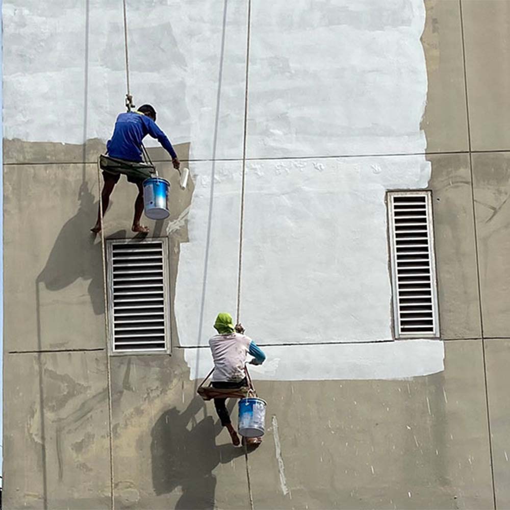 two painters painting a building wall while hanging on scaffolding