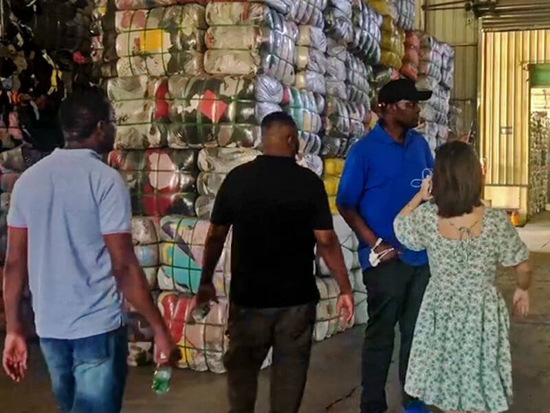 visiting customers in front of a large stack of used clothing bales