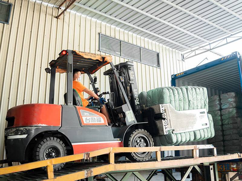 forklift operator loading a container with bales of used clothing